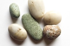 Six stones of indeterminate size in a range of colours - 3 white, 2 green, 1 pink - sit against a white background.